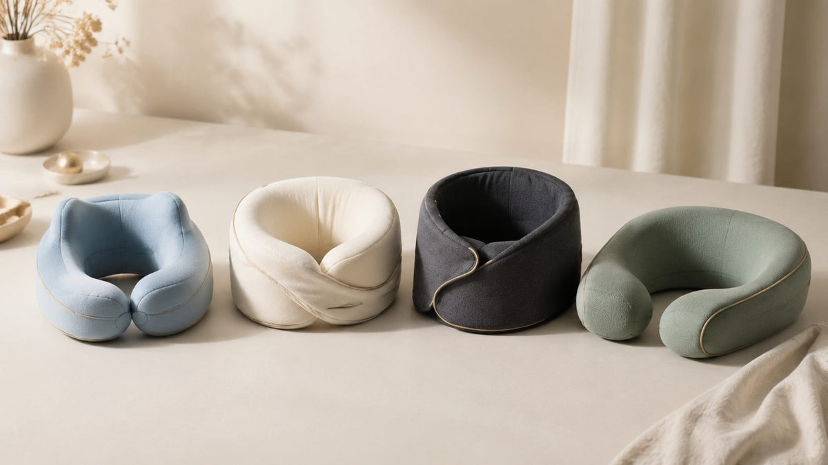 Four travel neck pillows lined up side by side in blue, cream, black and sage green
